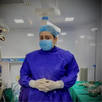 Dr. S Sanjana Devi in surgical scrubs and mask, standing in an operating theatre